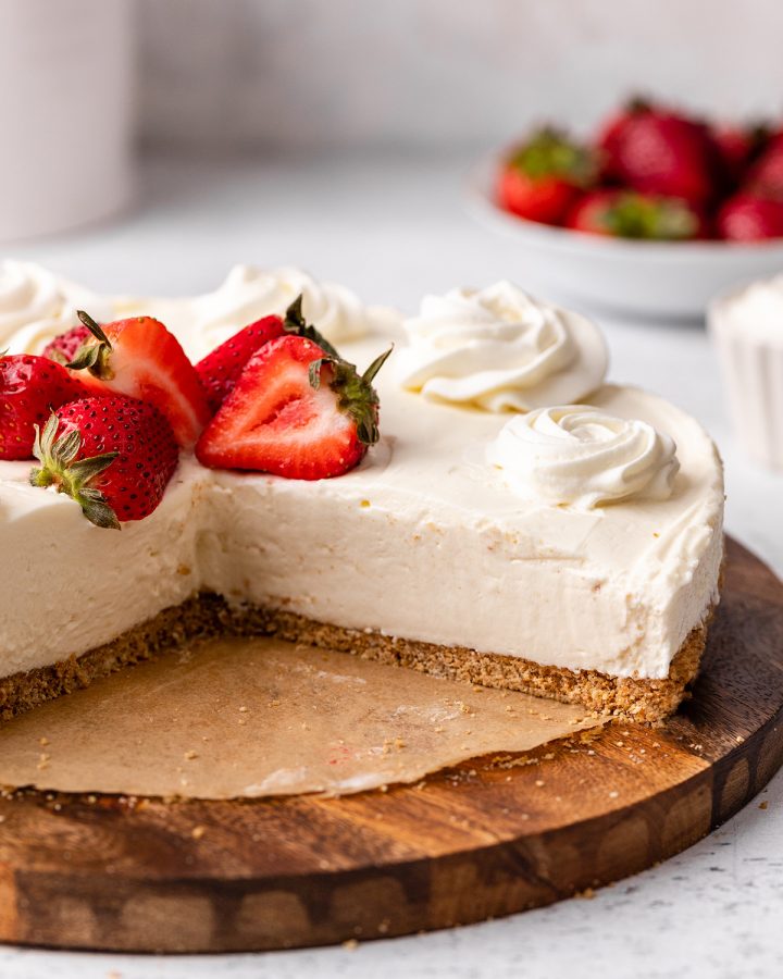 a No Bake Cheesecake with slices cut out of it topped with strawberries and whipped cream. 