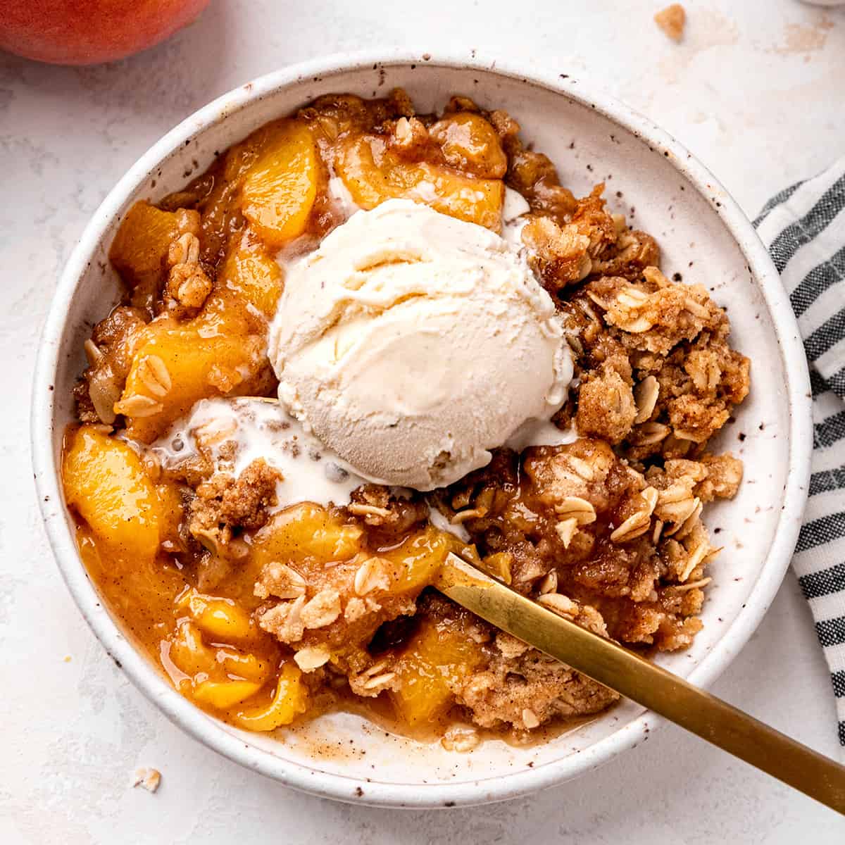 Peach Crisp in a bowl topped with vanilla ice cream