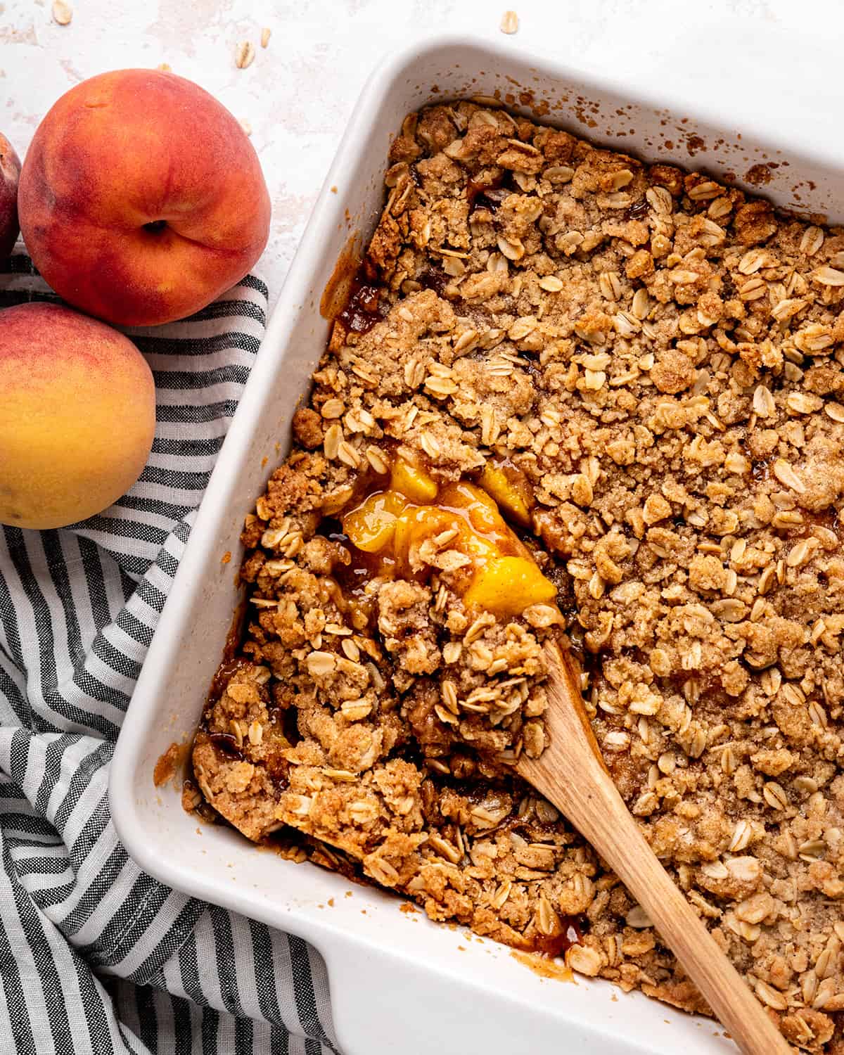 Peach Crisp Recipe in a baking dish with a wooden spoon