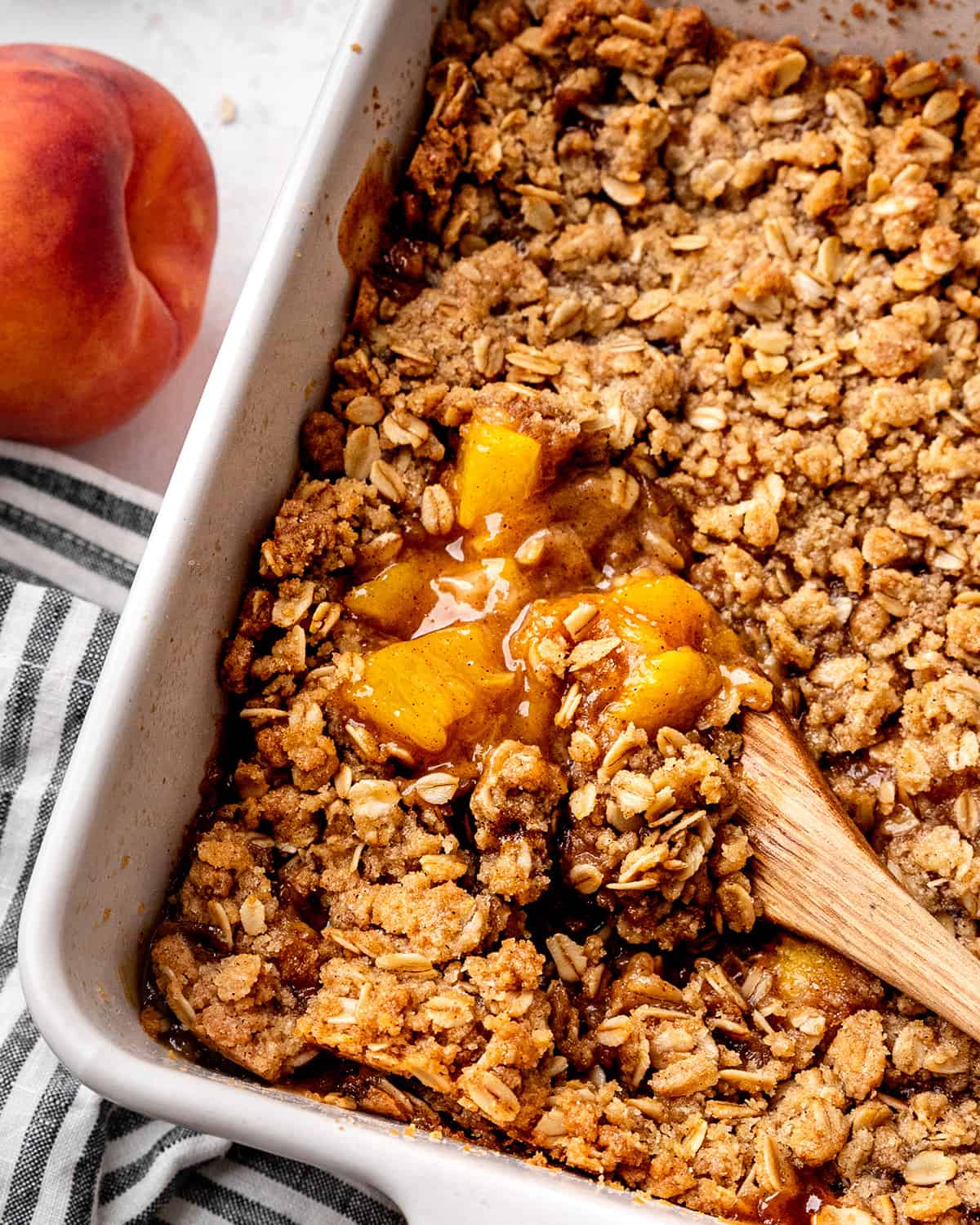 Peach Crisp in a baking dish with a wooden spoon