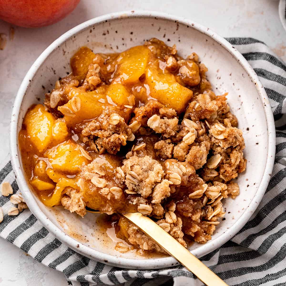 a bowl of peach crisp with a spoon 