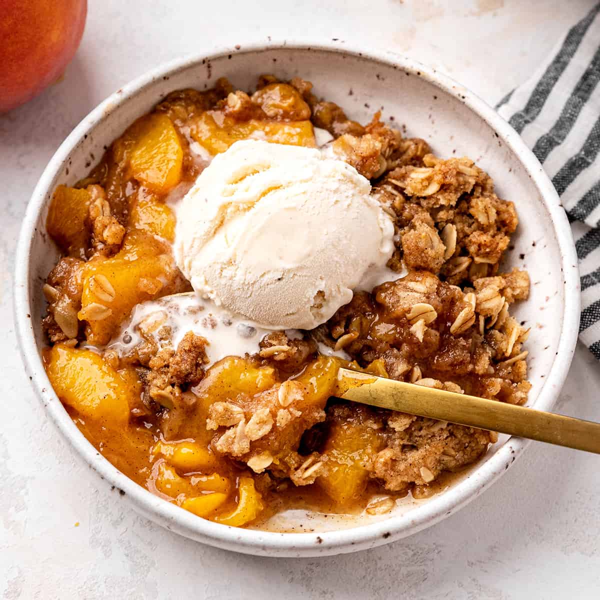 a bowl of peach crisp with vanilla ice cream and a spoon