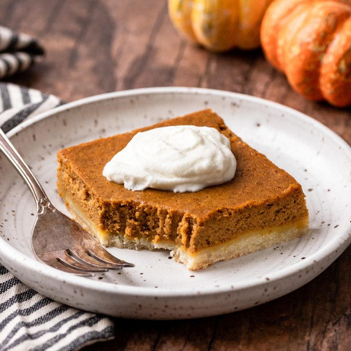 a Pumpkin Pie Bar on a plate with a bite taken out of it topped with whipped cream
