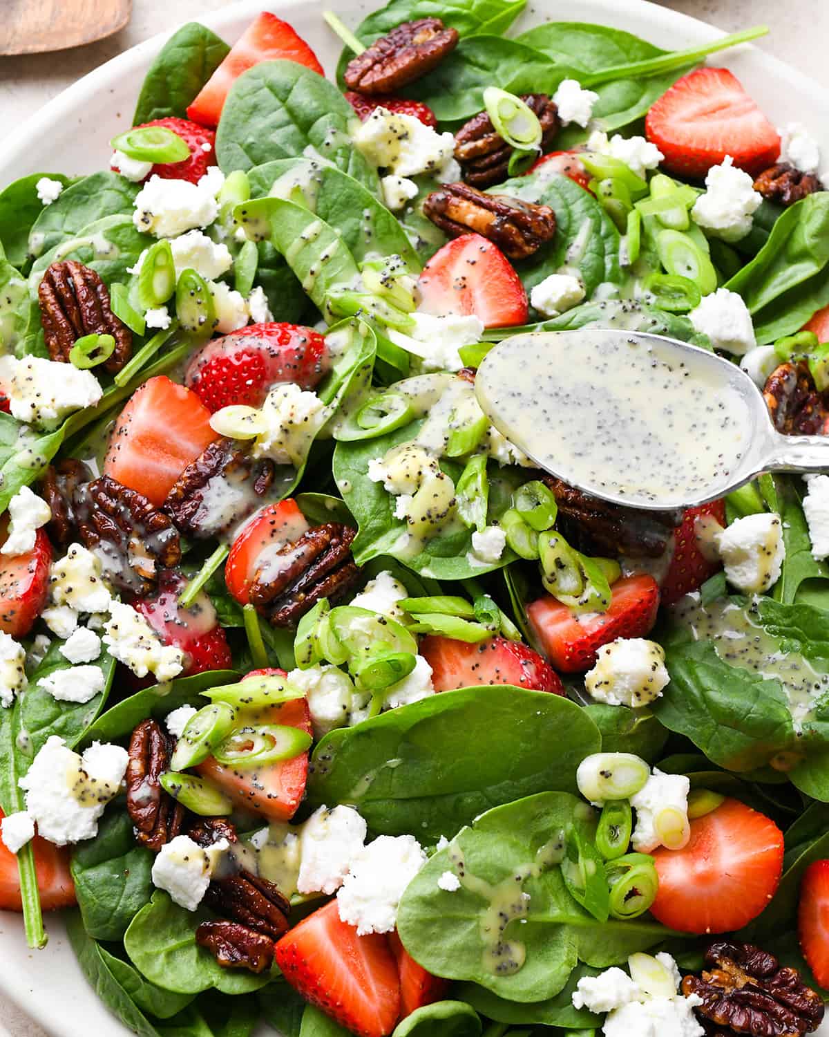 dressing being poured over a Strawberry Spinach Salad with a spoon