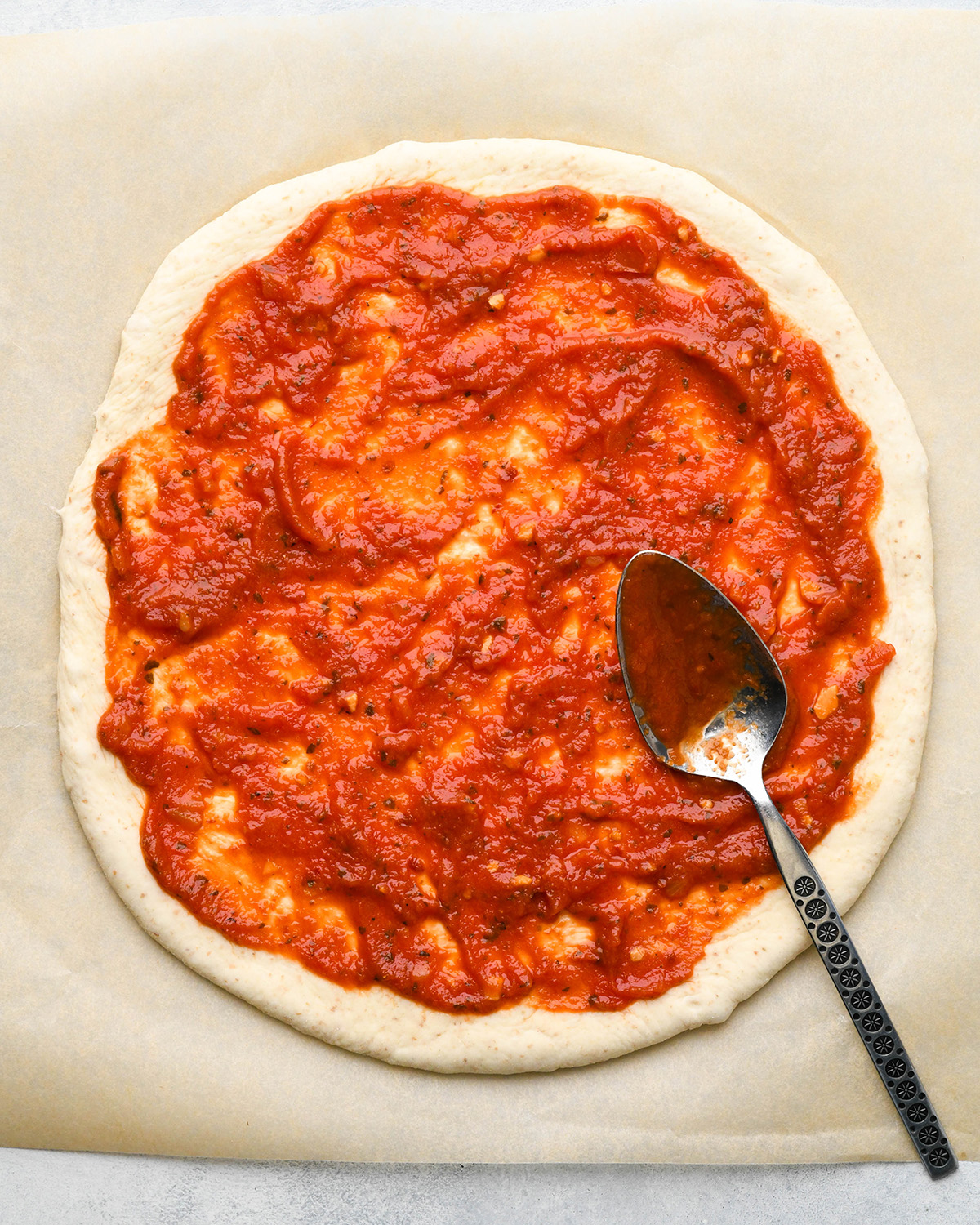 spreading sauce onto pizza dough to make BBQ Chicken Pizza Recipe