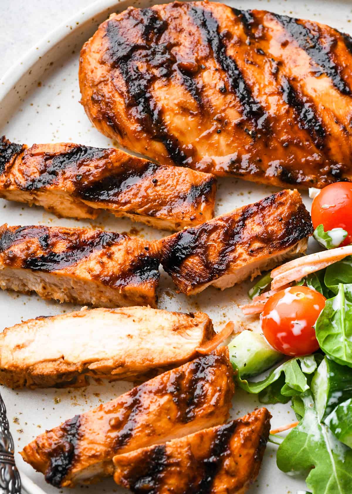2 grilled bbq chicken breasts on a plate with a salad, one cut into strips