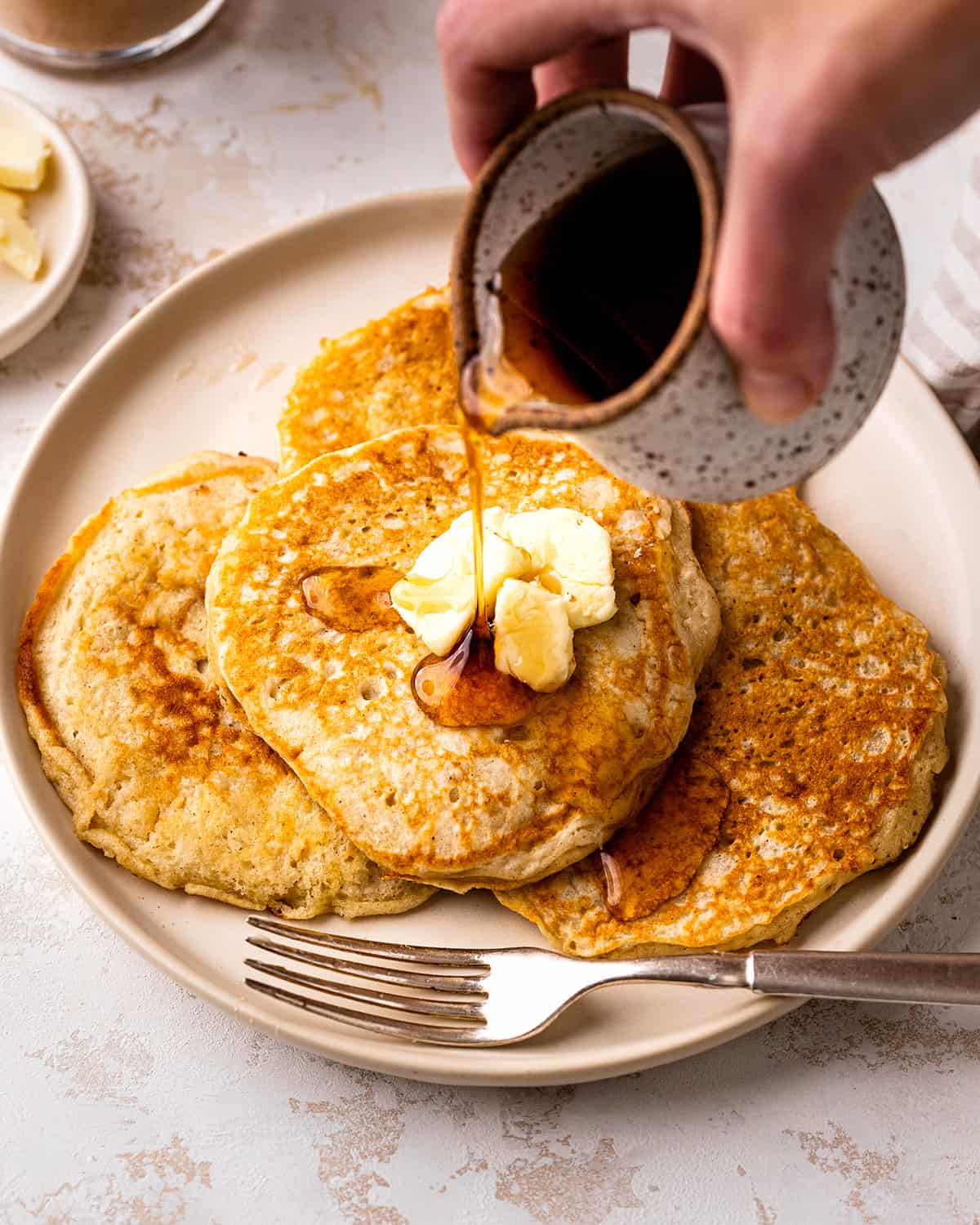 syrup being poured over 4 Buttermilk Pancakes on a plate with butter
