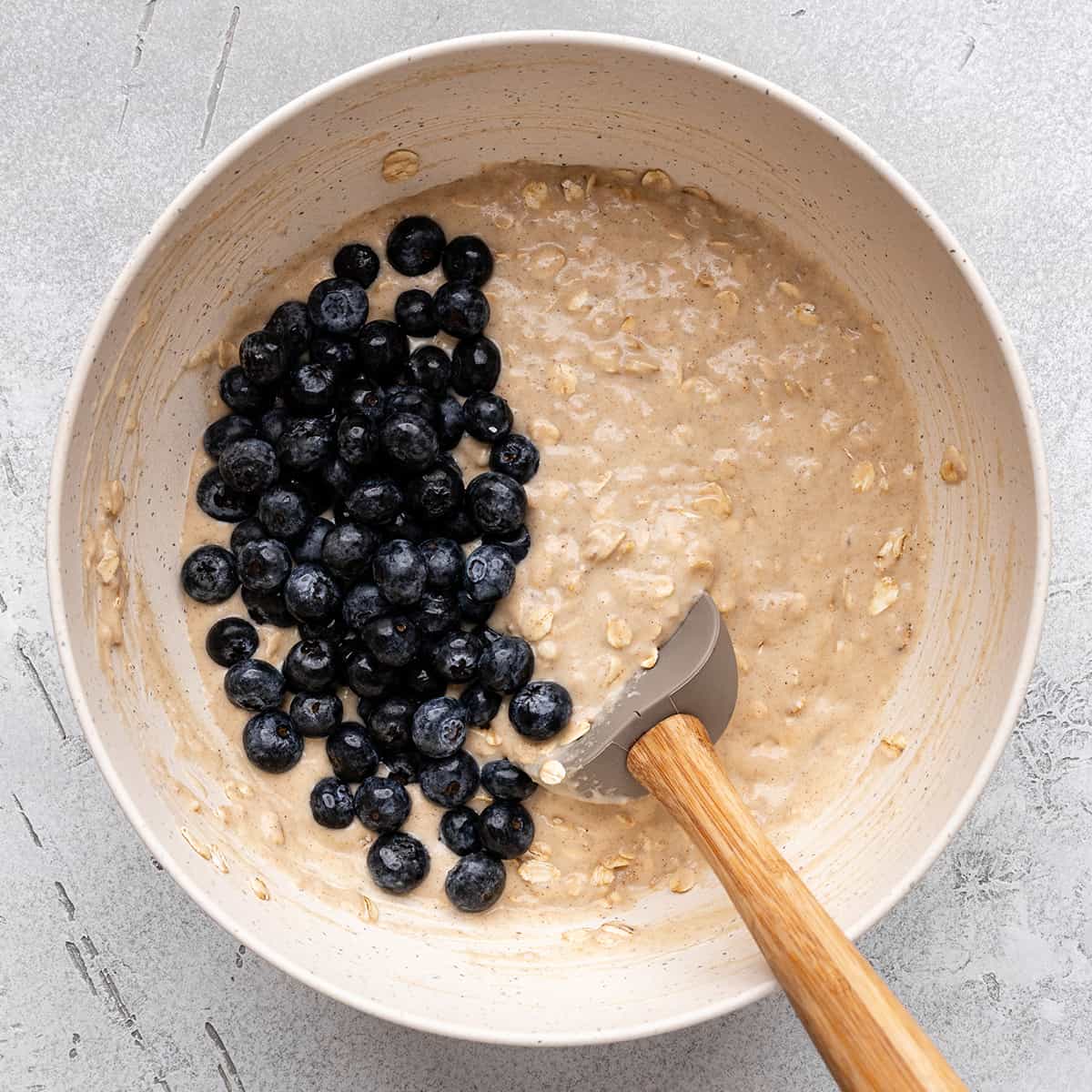 blueberries added to the blueberry oatmeal muffin batter in a bowl with a spatula