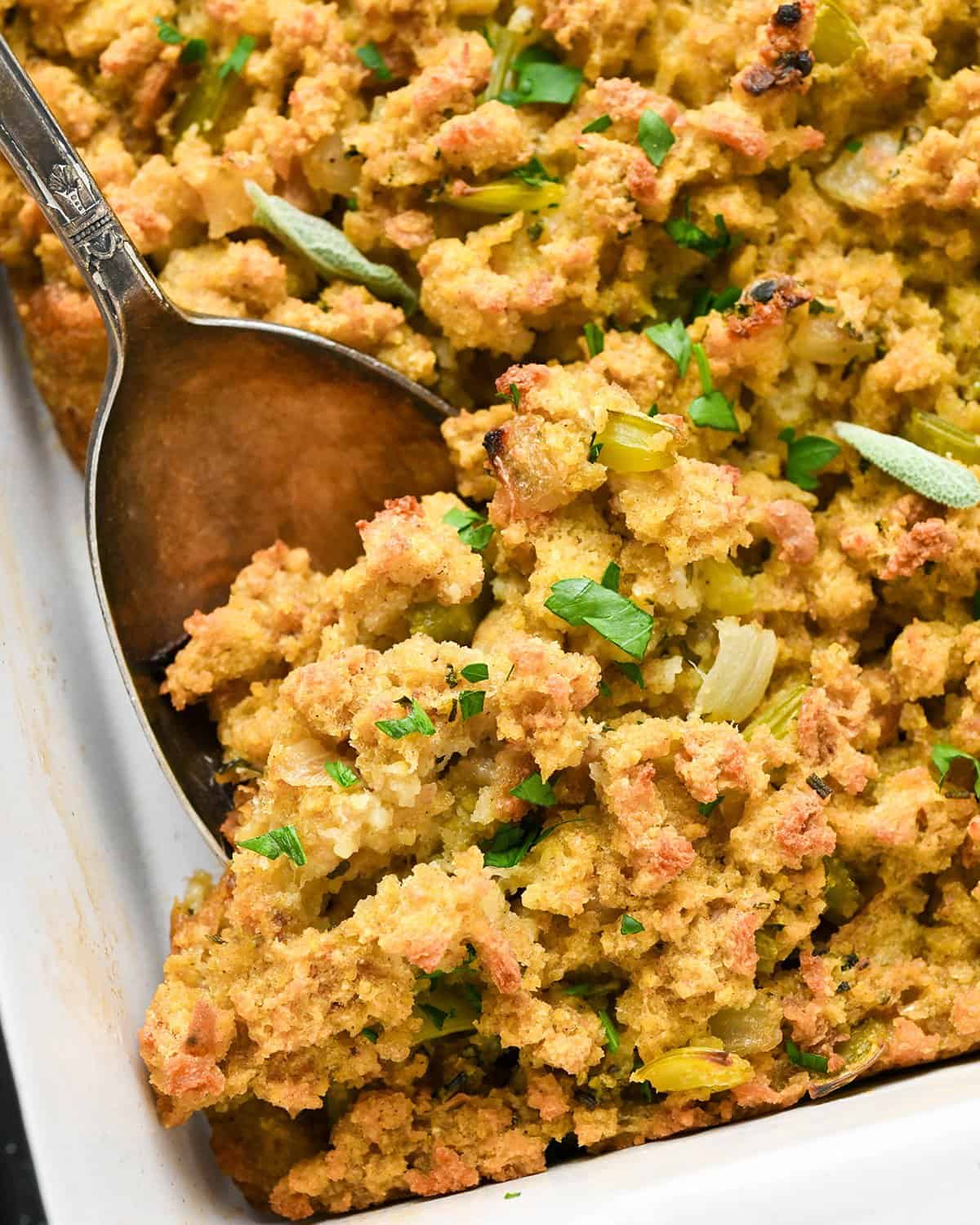 up close photo of a spoon taking a scoop of Cornbread stuffing out of a baking dish 