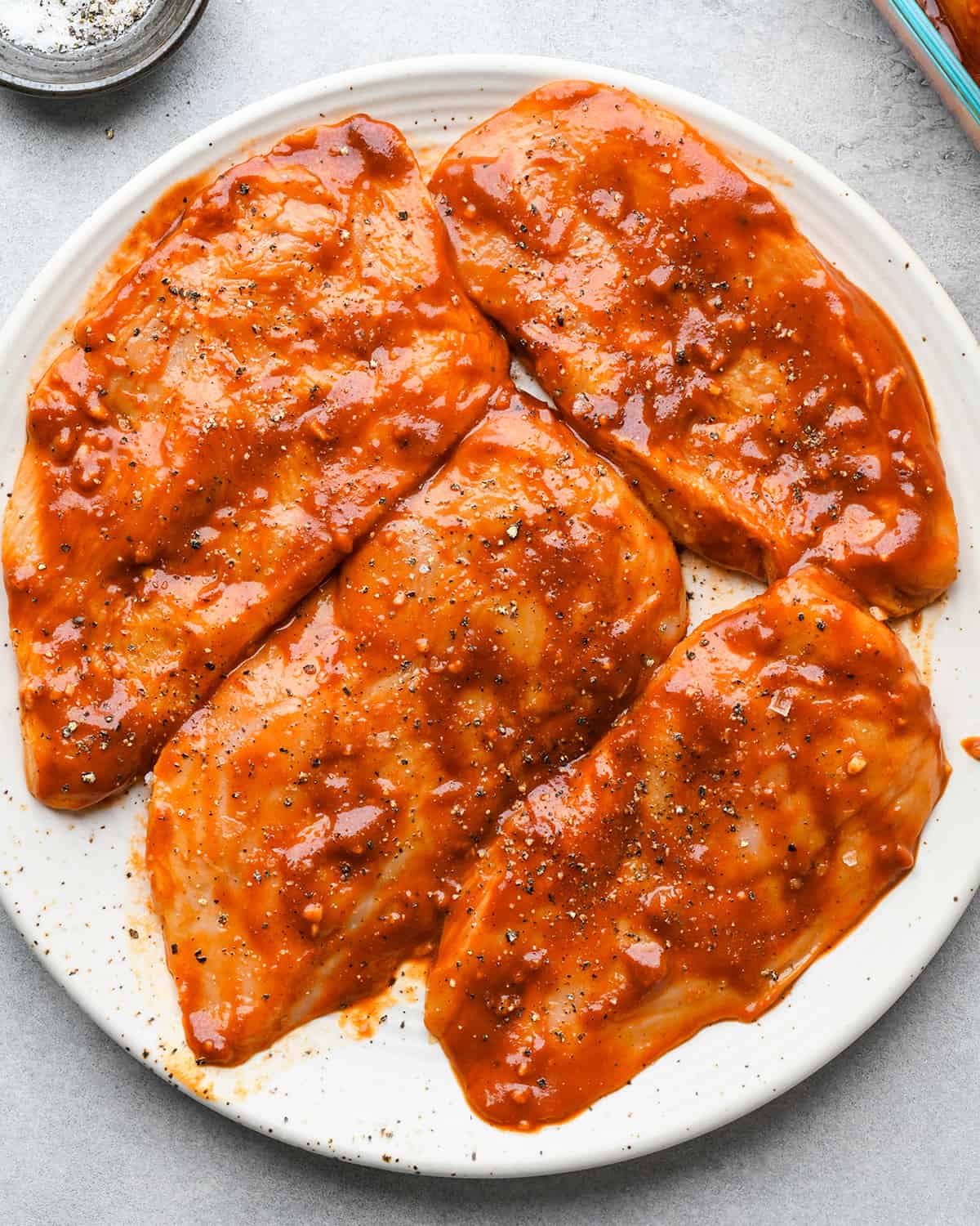 How to Make BBQ Chicken - marinated chicken breasts on a plate with salt and pepper