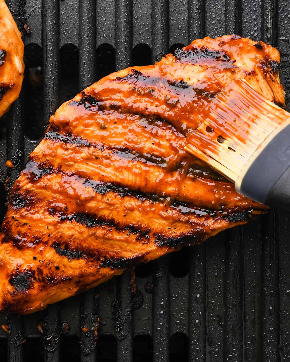 How to Make BBQ Chicken - BBQ sauce being brushed onto a chicken breast on the grill