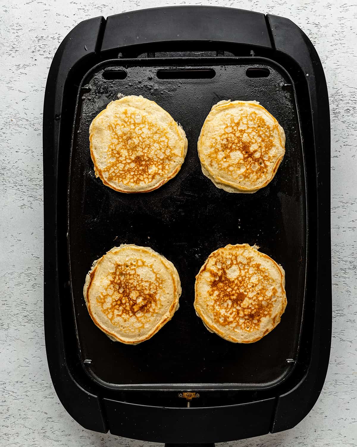4 buttermilk pancakes cooking on an electric griddle on the second side
