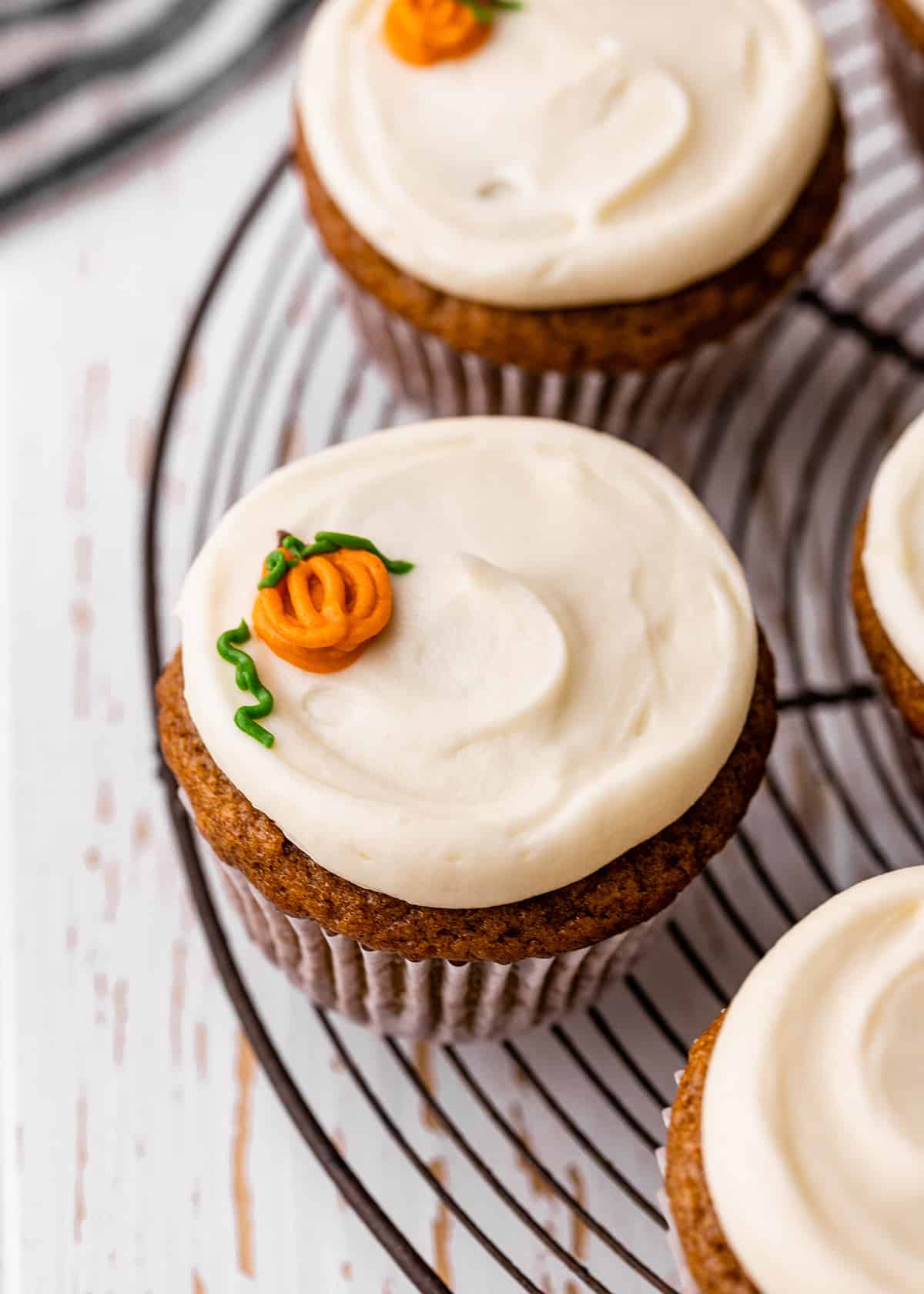 3 Pumpkin Cupcakes with cream cheese frosting on a wire rack