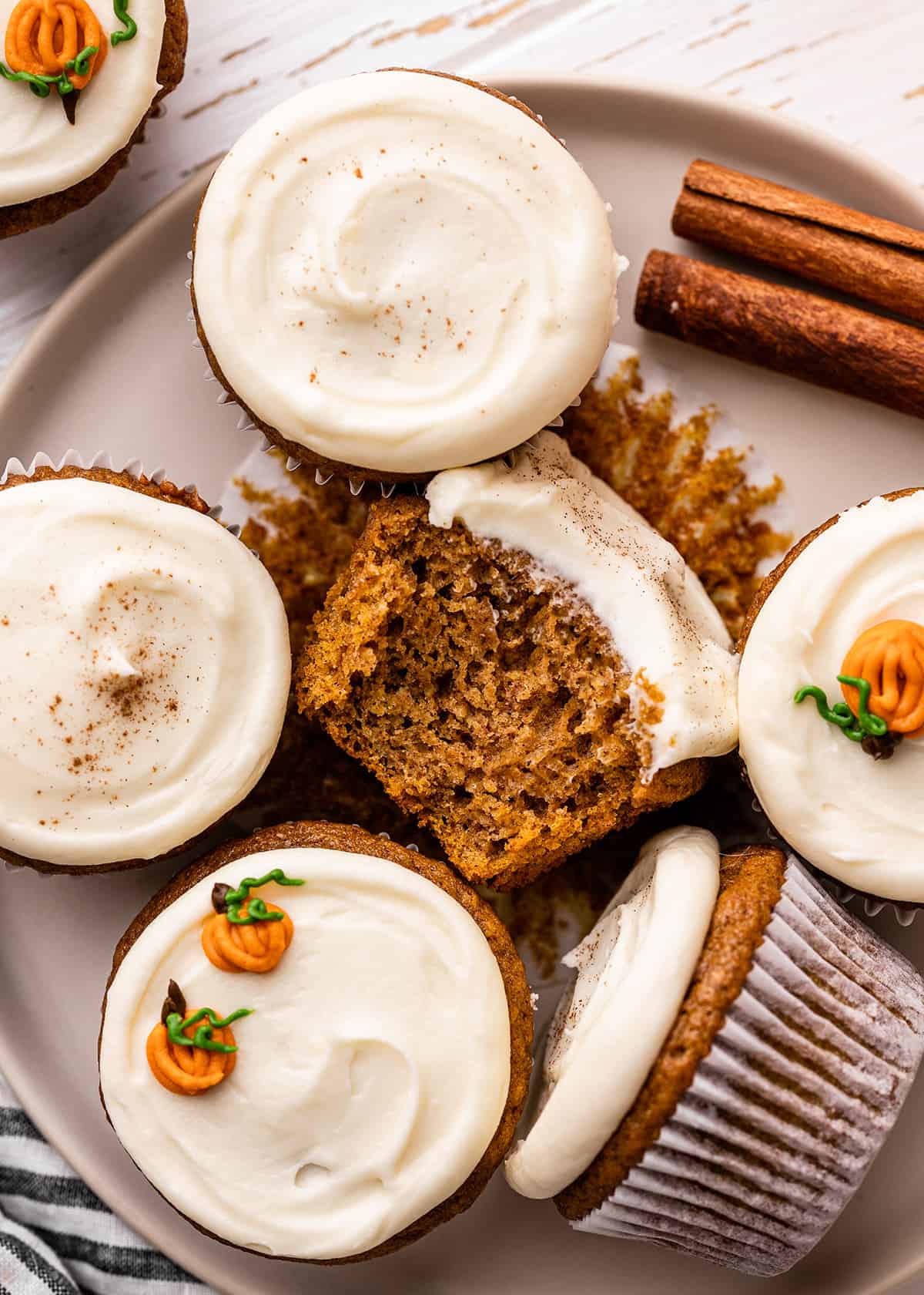 6 Pumpkin Cupcakes with cream cheese frosting, one with a bite taken out of it 