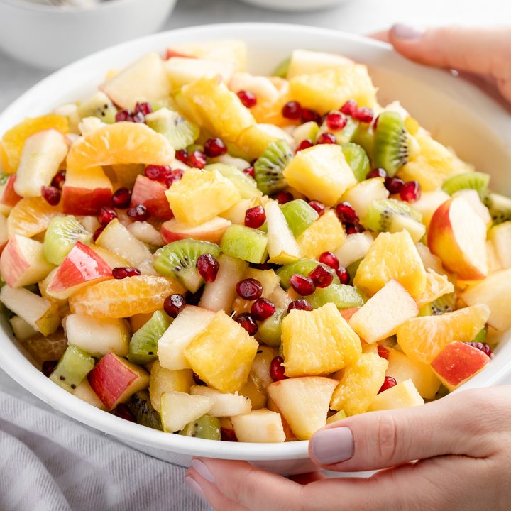 hands holding a serving bowl full of Winter Fruit Salad
