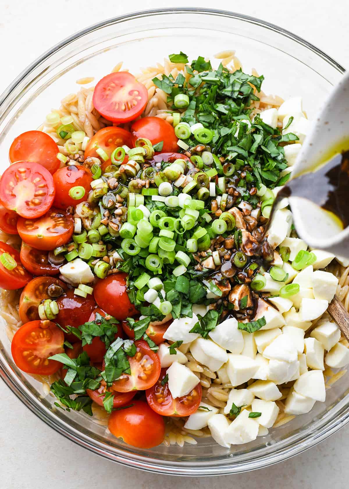 dressing pouring over Caprese Orzo Salad in a bowl