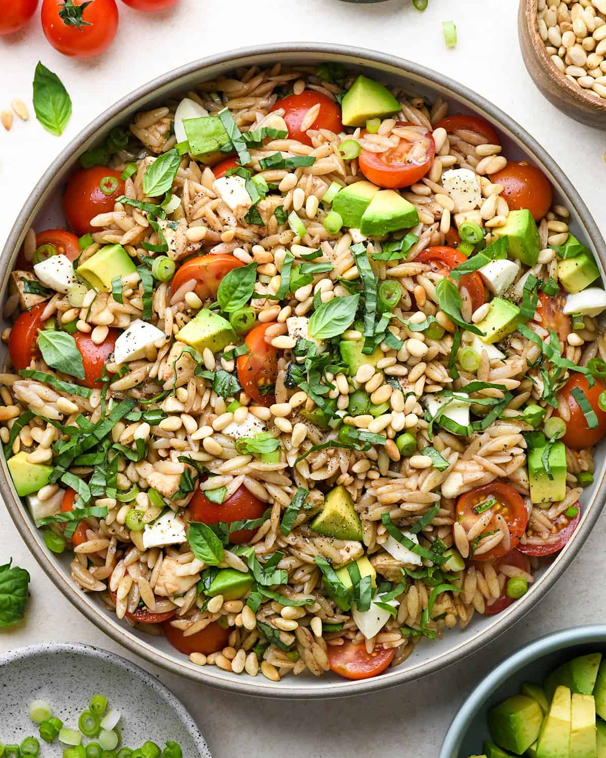Caprese Orzo Salad in a serving bowl garnished with pine nuts and avocado