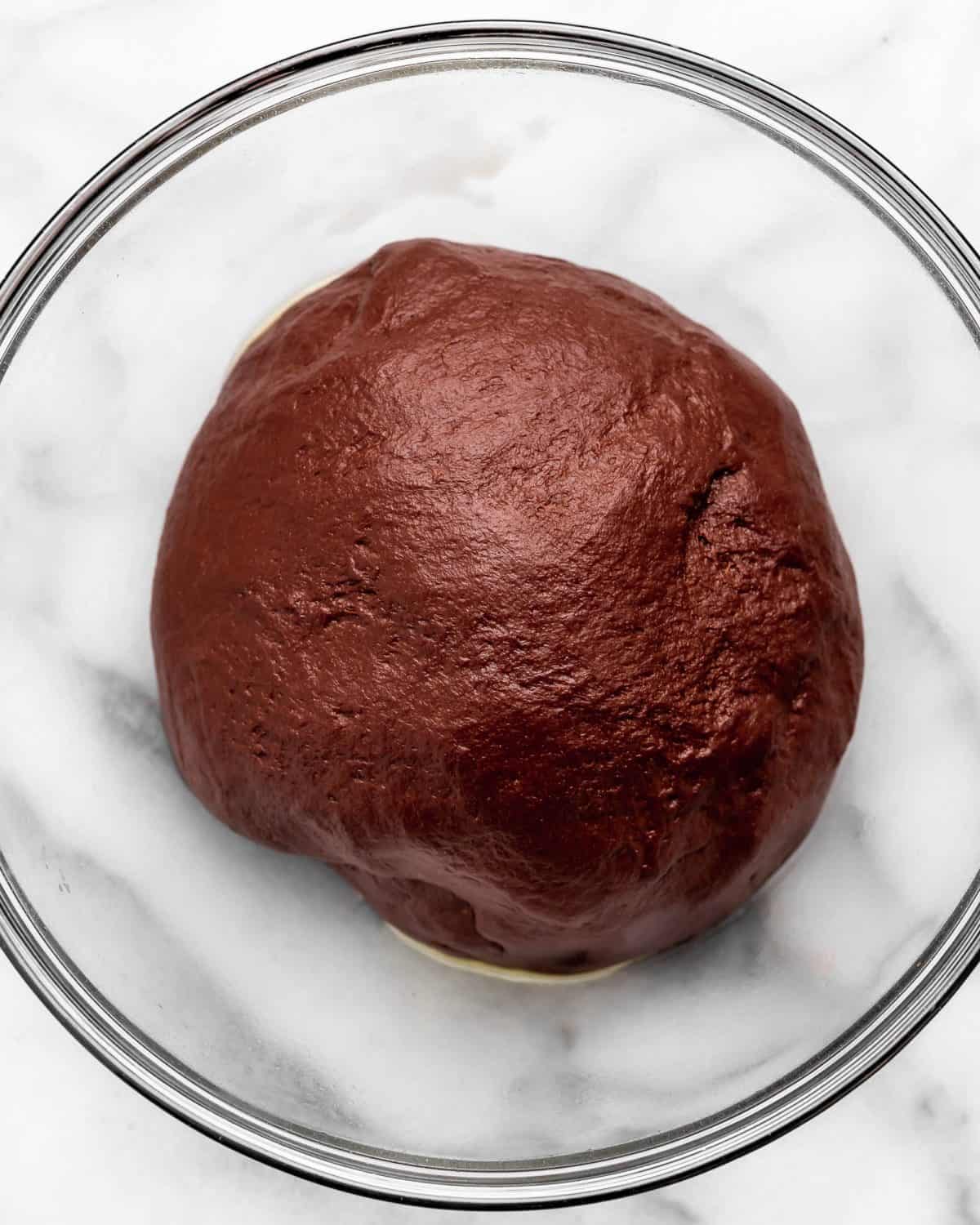 making chocolate cinnamon rolls - dough in a glass bowl on a marble surface after rising