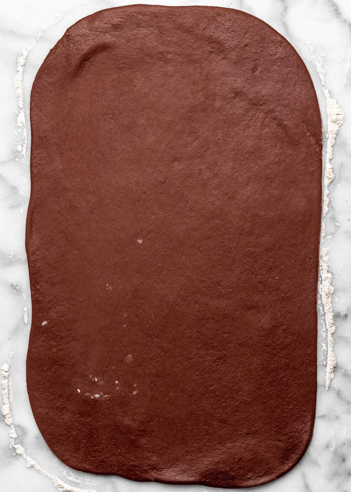 making chocolate cinnamon rolls - dough rolled into a large rectangle on a floured marble surface