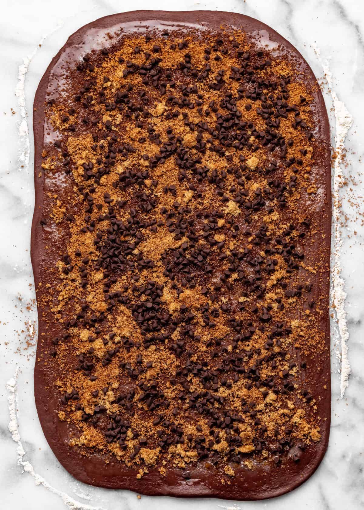 making chocolate cinnamon rolls - dough rolled into a large rectangle and covered in melted butter, cinnamon sugar filling and mini chocolate chips