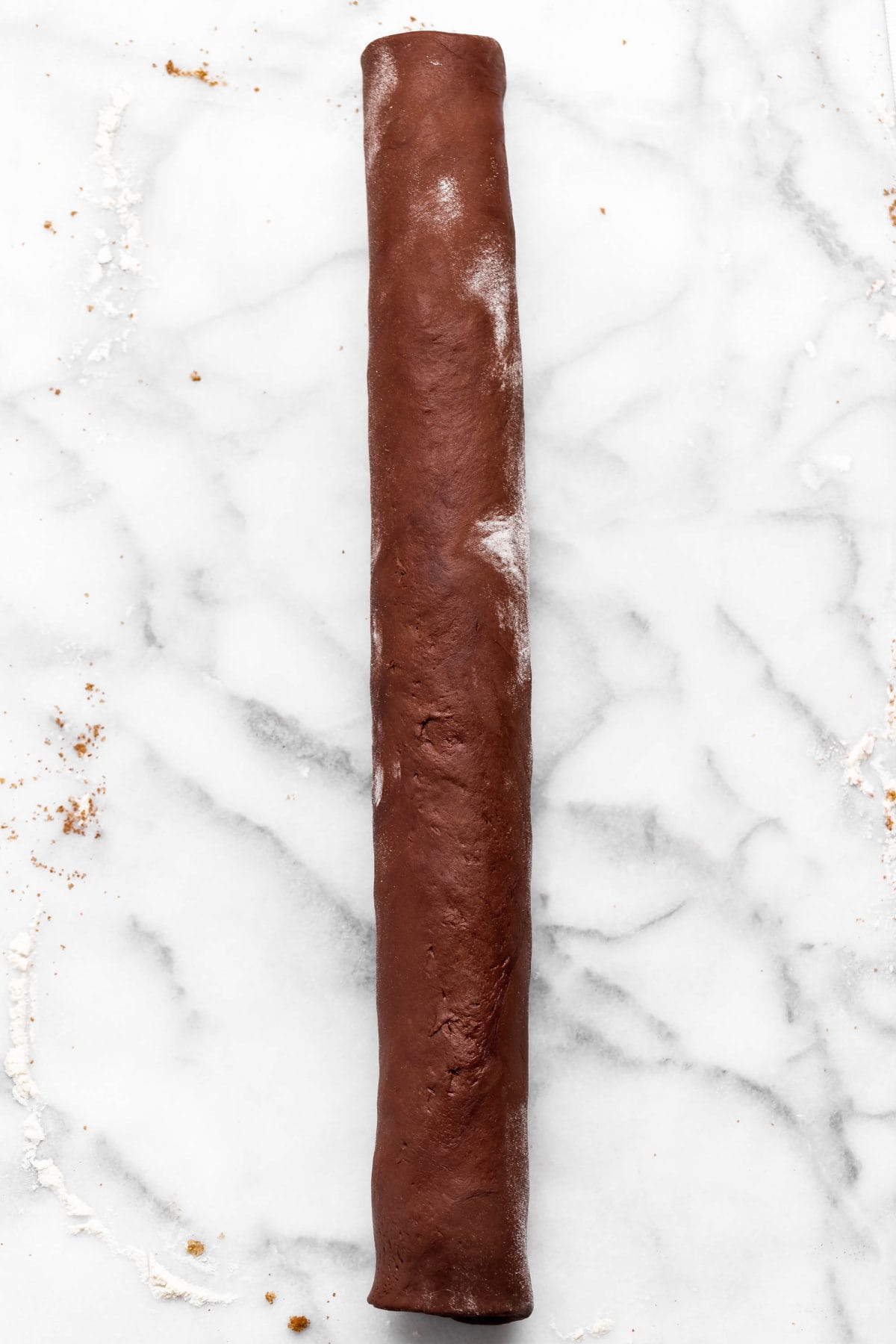 making chocolate cinnamon rolls - filled dough rolled into a long log on a floured marble surface