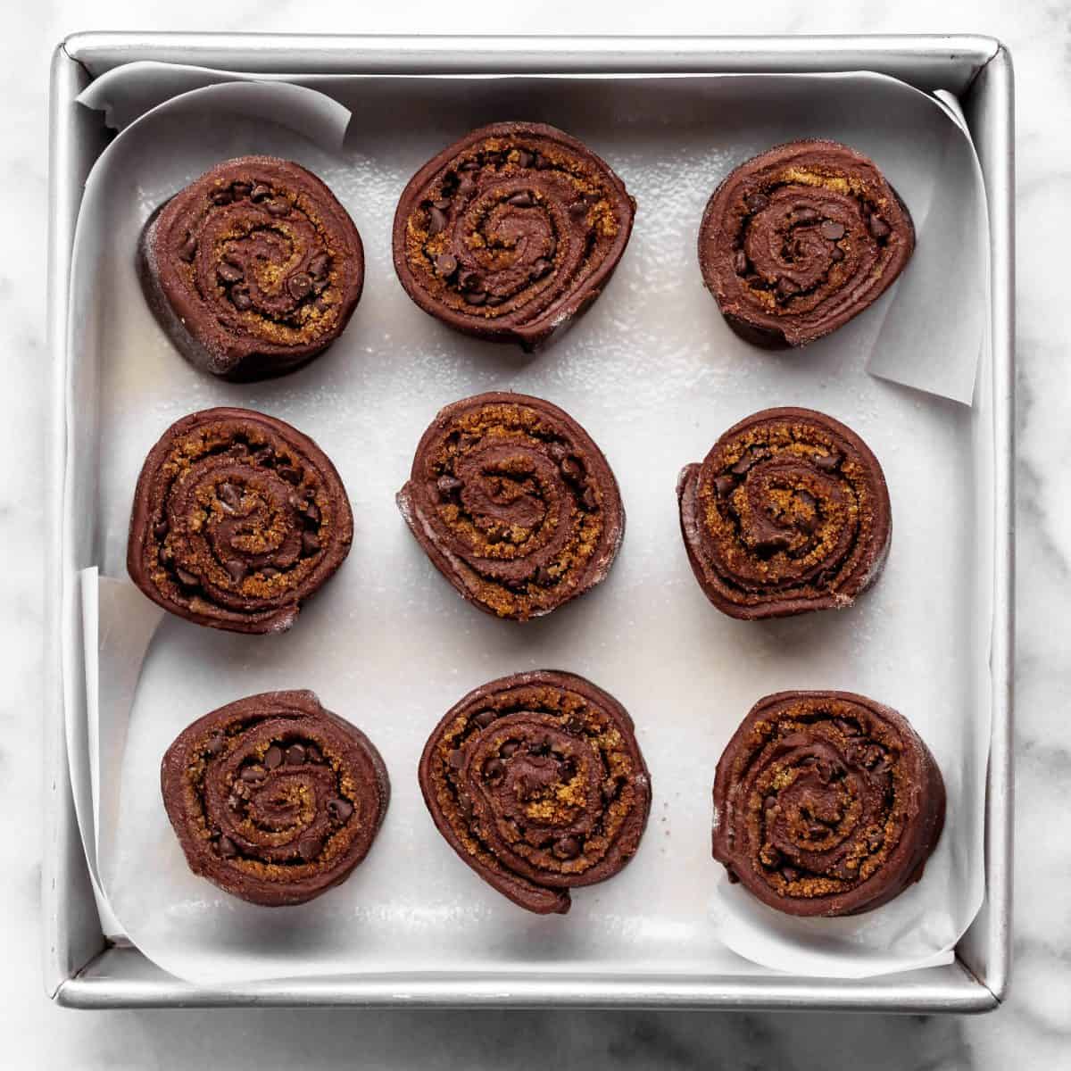 9 chocolate cinnamon rolls in a square metal baking dish lined with parchment paper before baking