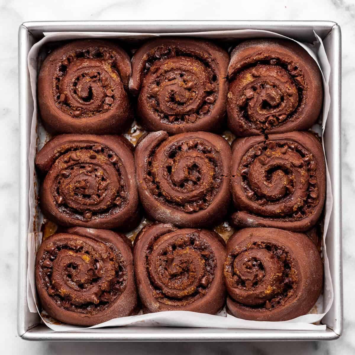 9 chocolate cinnamon rolls in a square metal baking dish lined with parchment paper after baking