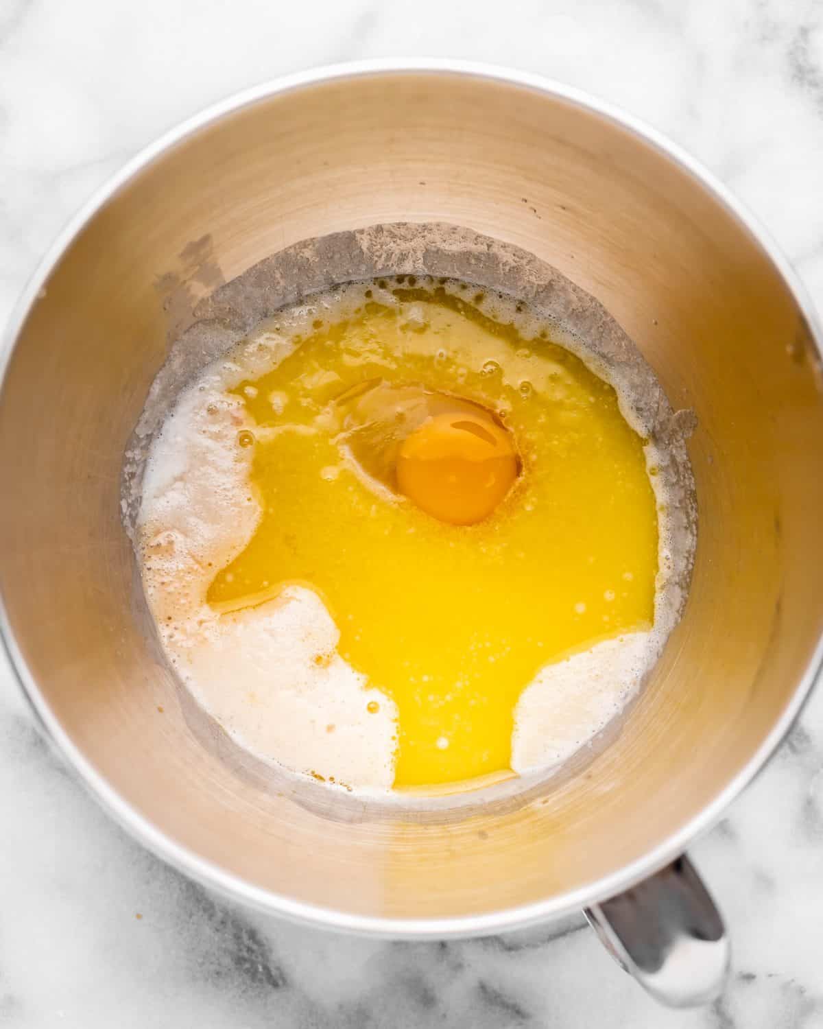 making chocolate cinnamon rolls - milk, sugar, butter, egg and vanilla added to the proofed yeast in a metal mixing bowl on a marble surface before mixing