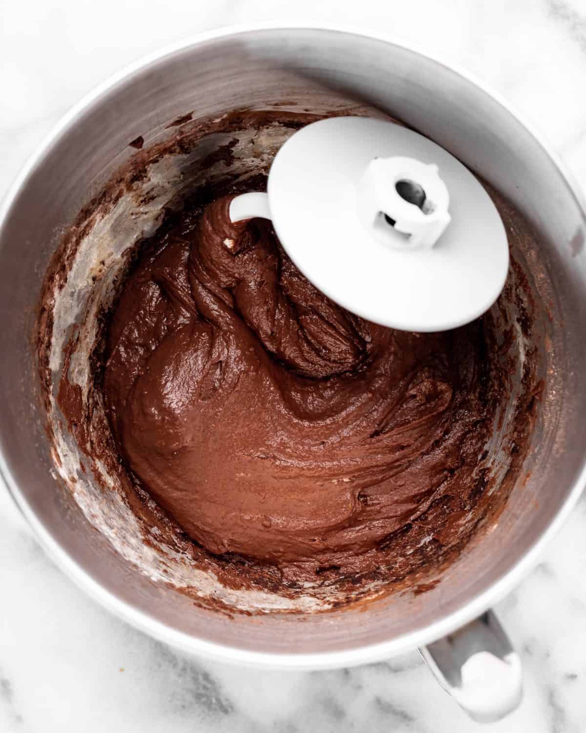 making chocolate cinnamon rolls - partially formed dough in a metal mixing bowl with a white dough hook in the dough on a metal surface