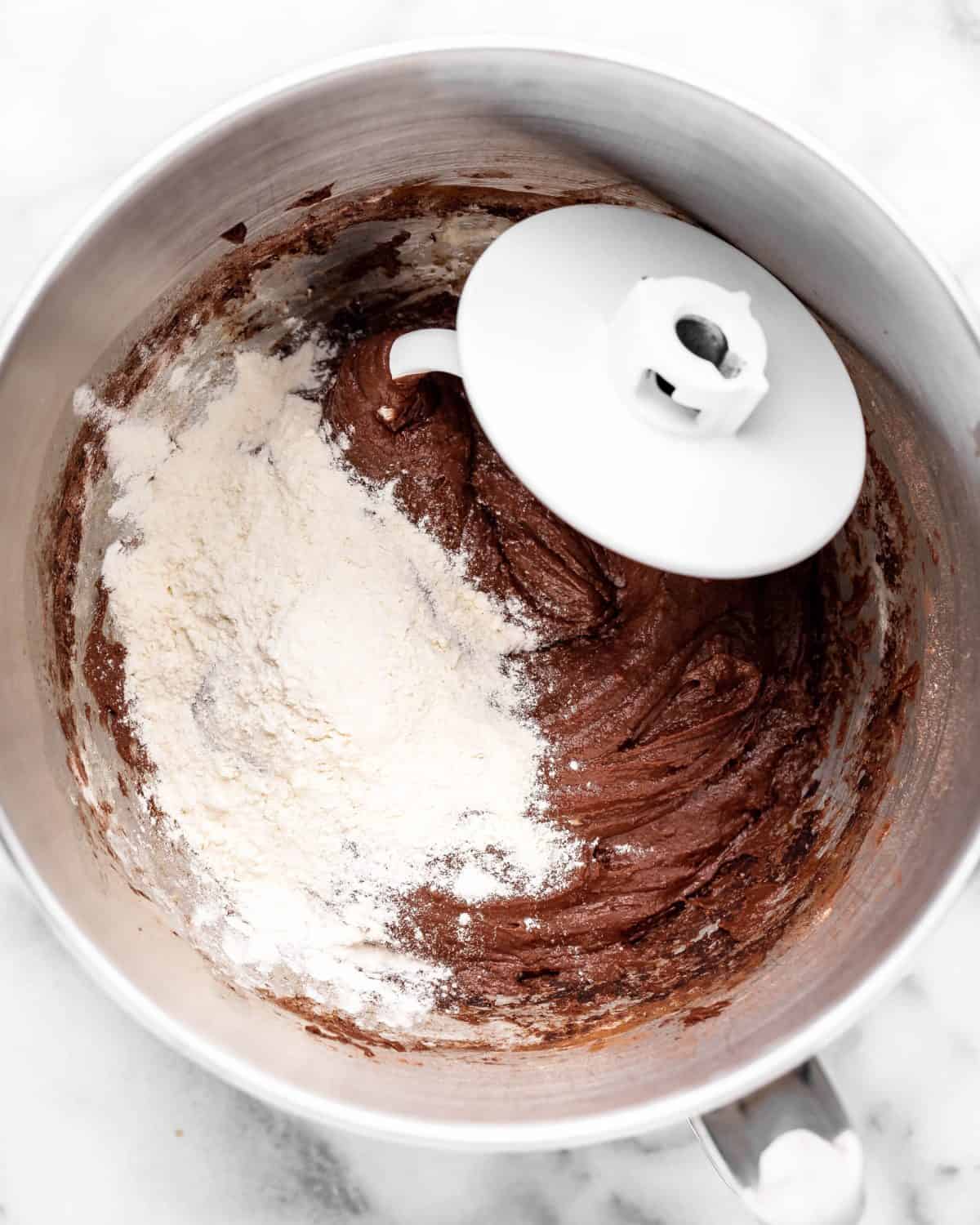 making chocolate cinnamon rolls - more flour added to the dough in a metal mixing bowl with a dough hook on a marble surface