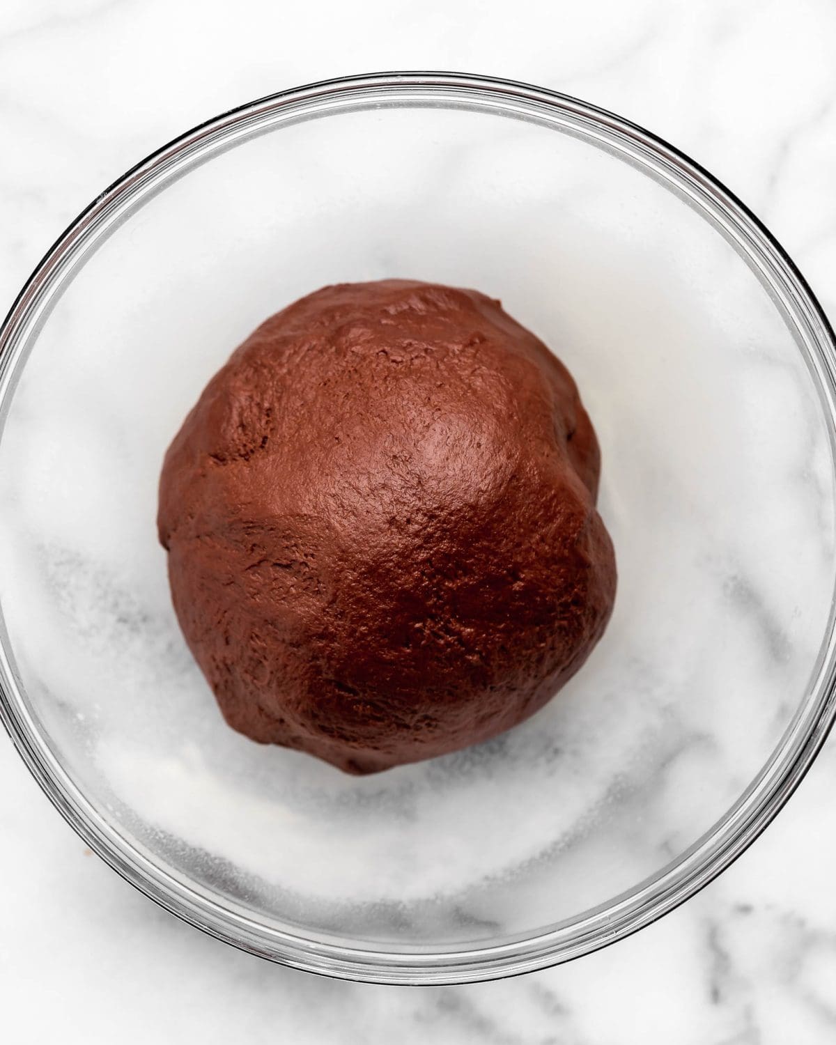 making chocolate cinnamon rolls - dough in a glass bowl on a marble surface before rising