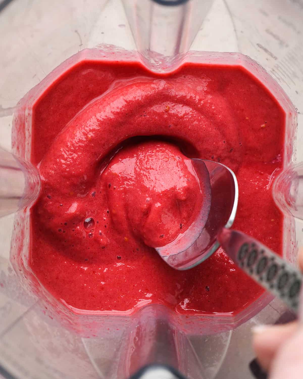 a spoon scooping some Raspberry Smoothie in a blending contianer after blending 