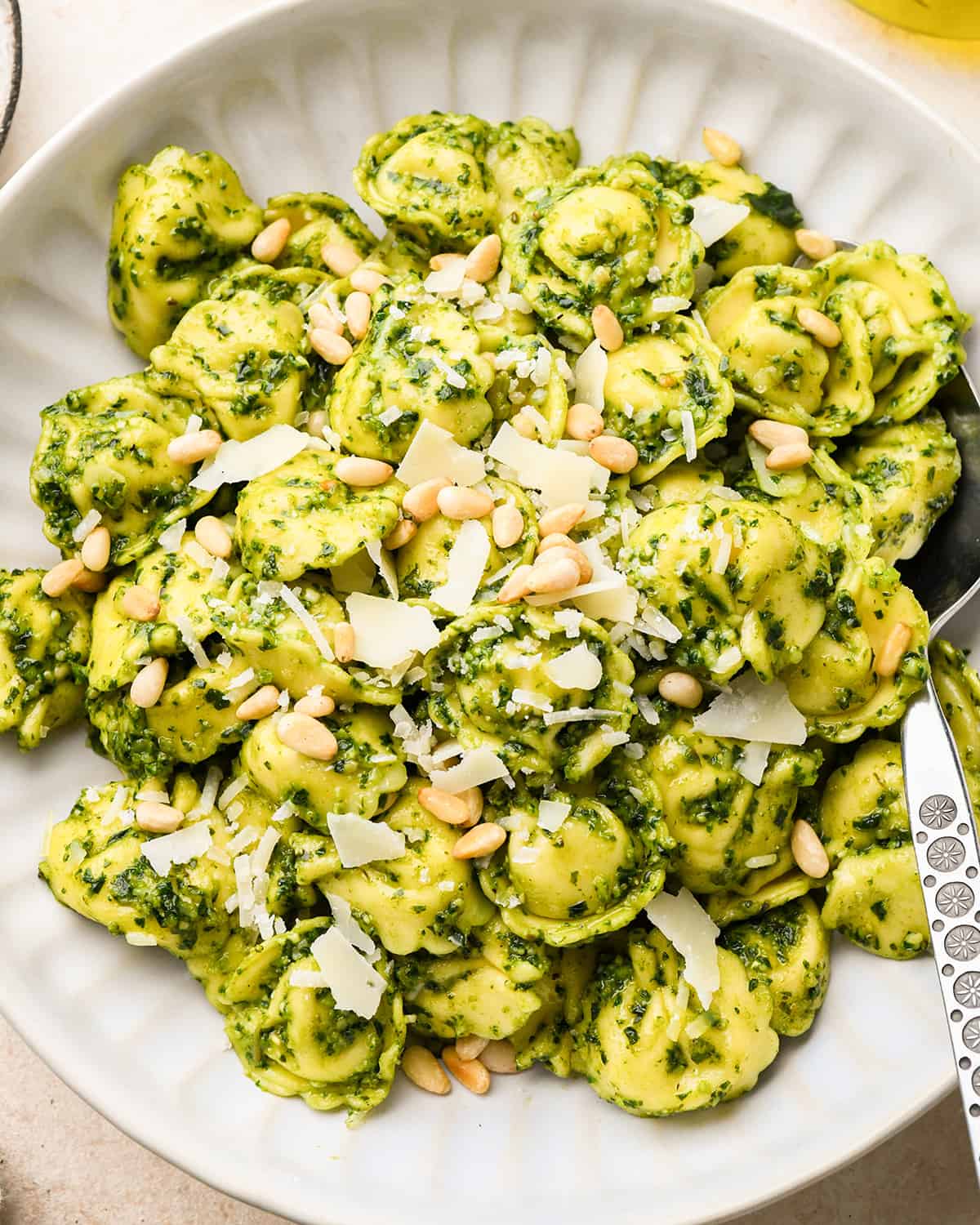 pesto tortellini topped with parmesan and pine nuts on a plate with a spoon