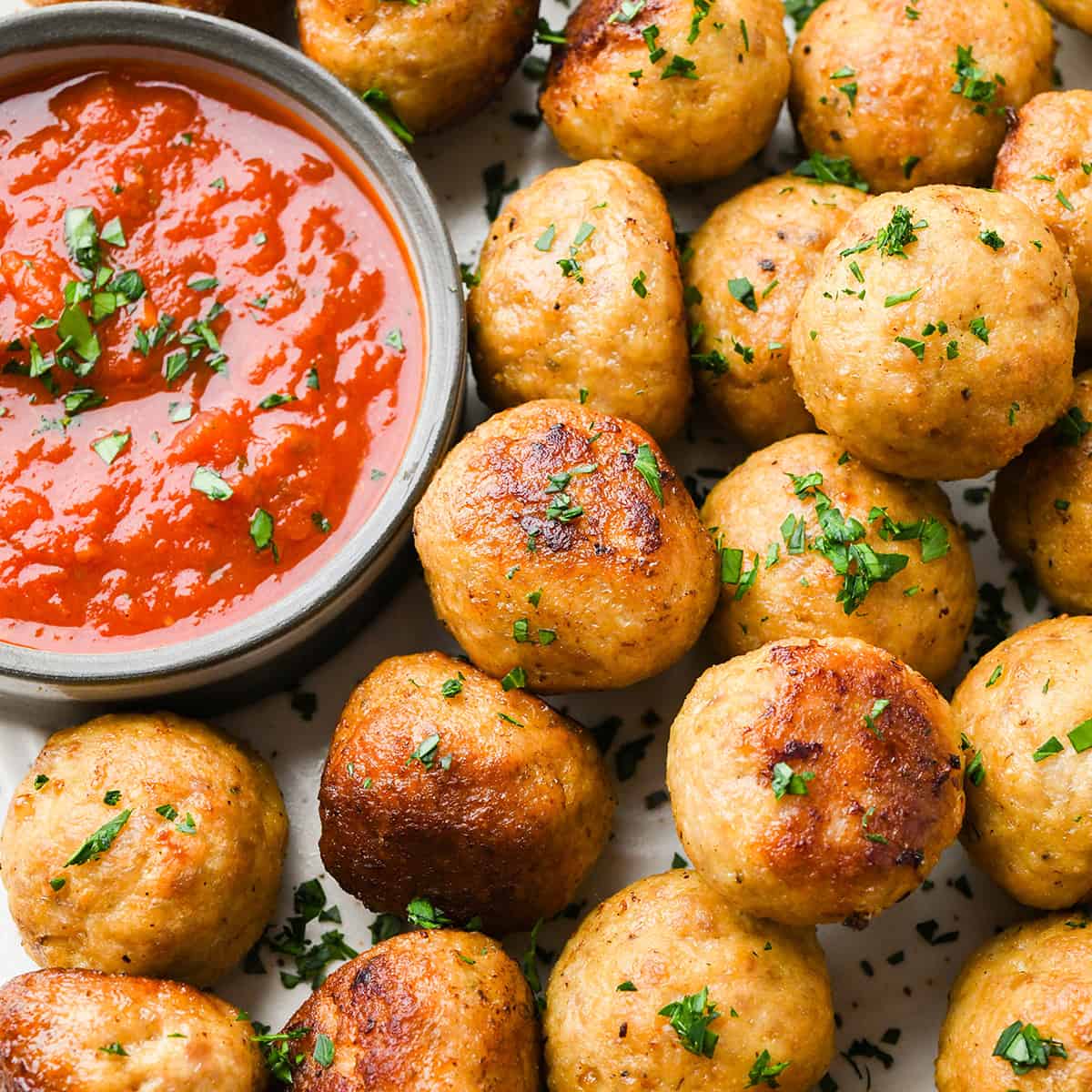 Chicken Meatballs garnished with parsley with a bowl of marinara sauce for dipping