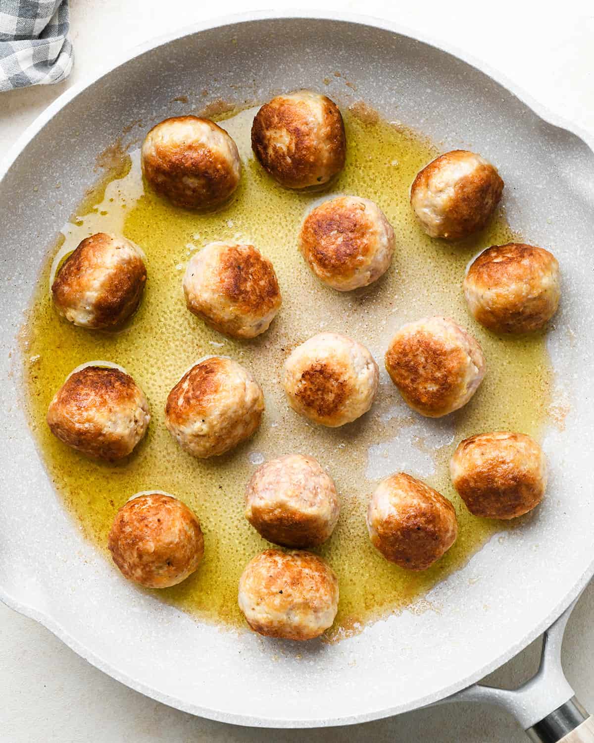 chicken meatballs cooking in olive oil in a skillet