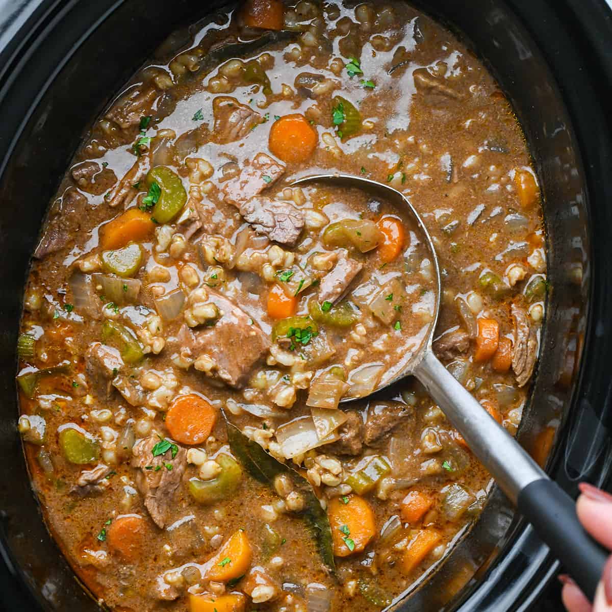 a ladle taking a scoop of Beef Barley Soup out of a slow cooker