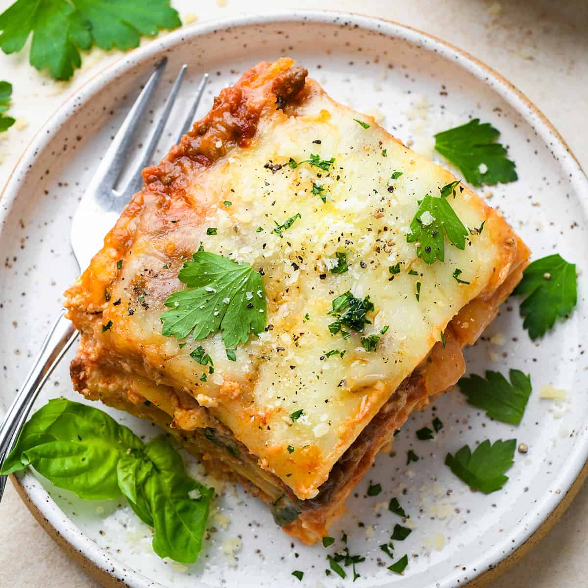 A piece of beef lasagna on a plate garnished with parsley and basil 