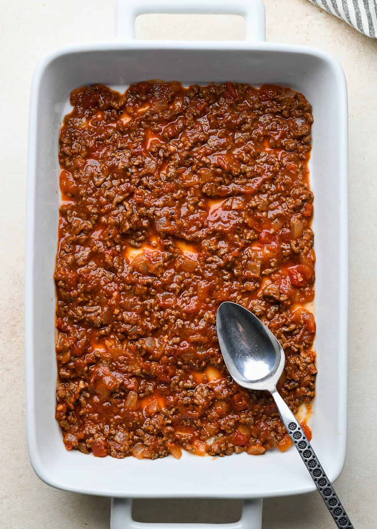 Spreading meat sauce in the bottom of a baking dish for beef lasagna