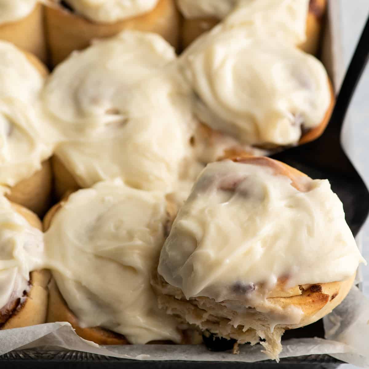 a cinnamon roll being lifted out of a baking pan with a pie server