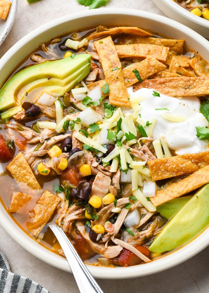 a bowl of Chicken Tortilla Soup topped with cheese and herbs and tortilla strips