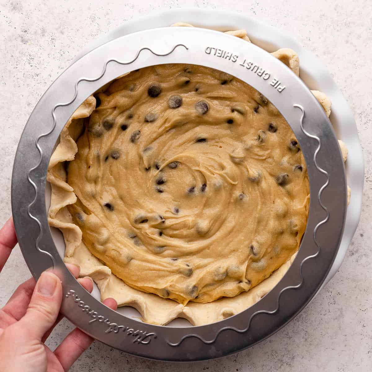 a pie crust shield being put over chocolate chip cookie pie in a pie dish before baking