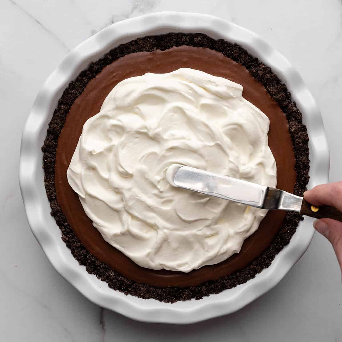 whipped cream being spread on top of the chocolate pudding pie filling