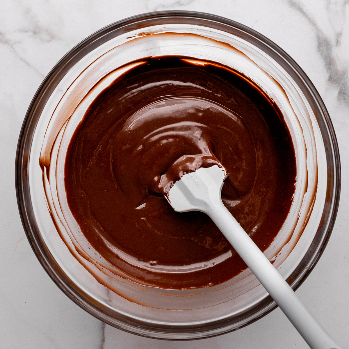 chocolate pudding pie mixture cooling in a glass bowl with a spatula