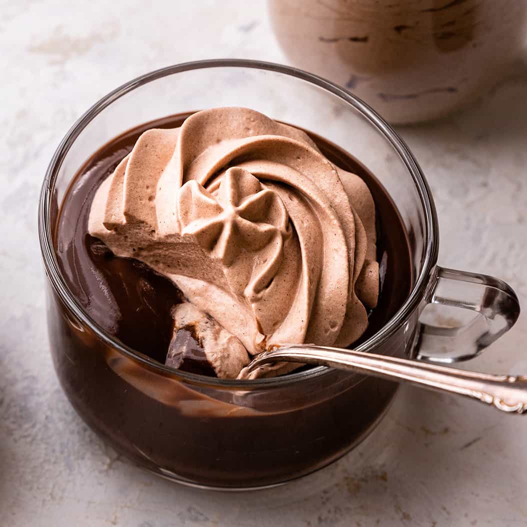 Chocolate Whipped Cream piped onto chocolate pudding in a glass cup with a spoon