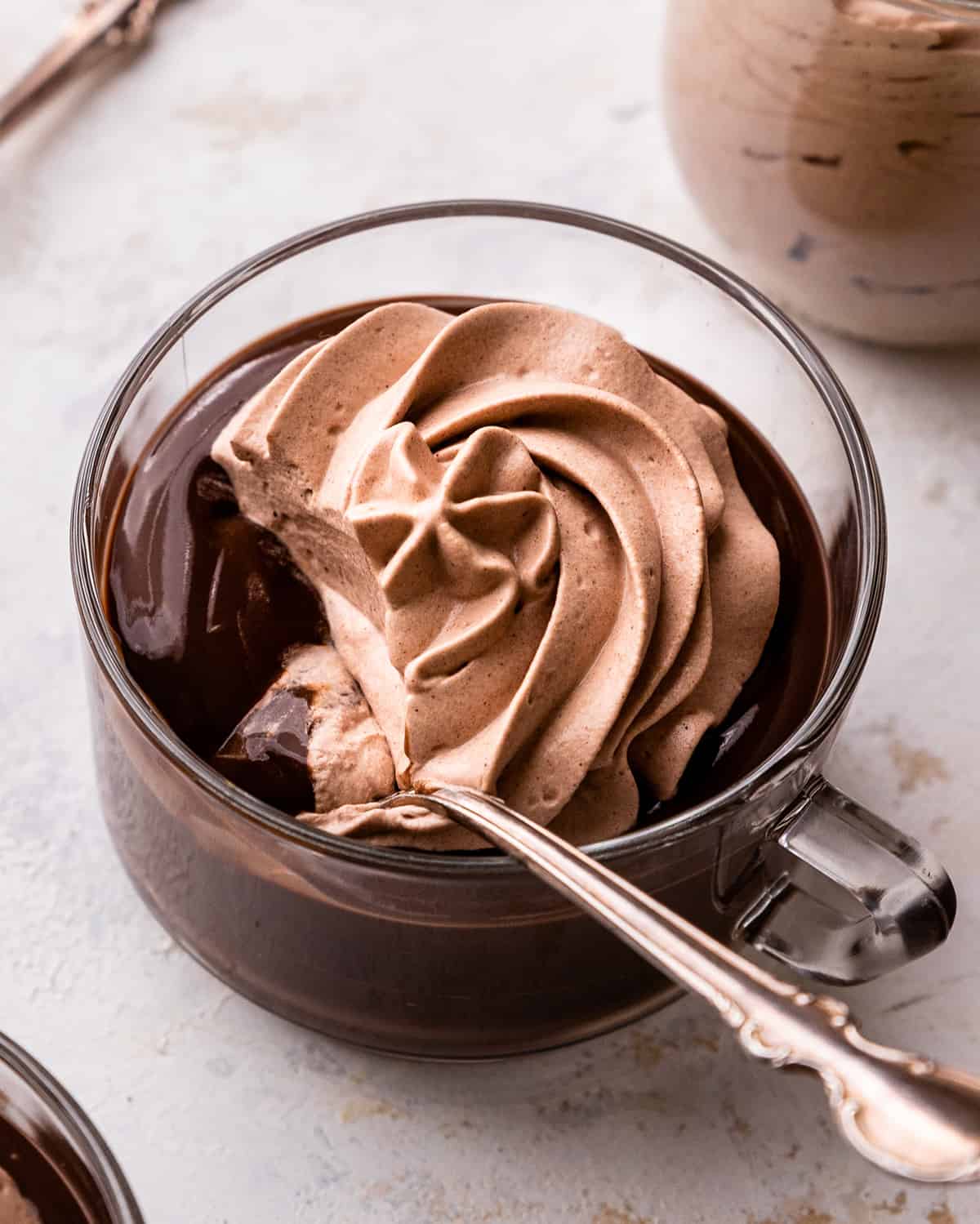 Chocolate Whipped Cream on top of chocolate pudding in a glass cup with a spoon 
