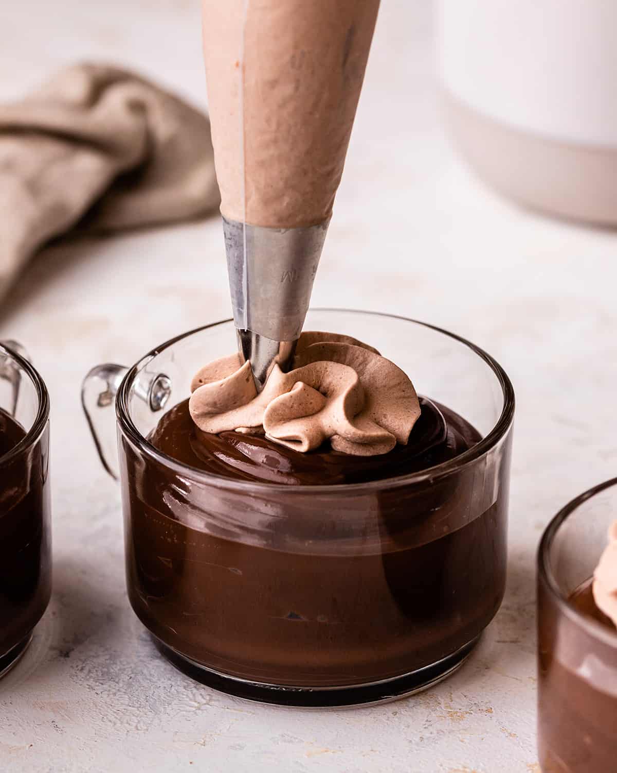 Chocolate Whipped Cream in a piping bag being piped onto chocolate pudding in a glass cup