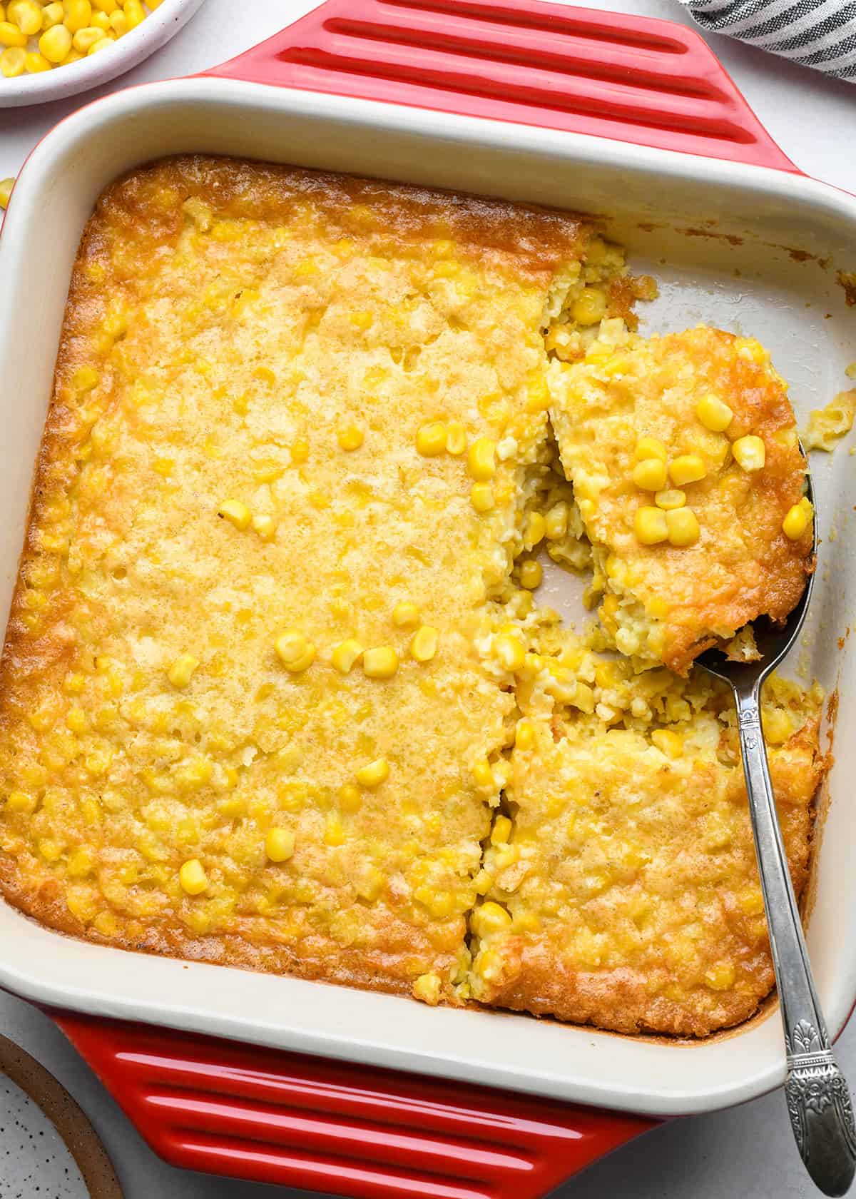 Corn Pudding in a baking dish with a spoon cut into pieces. 