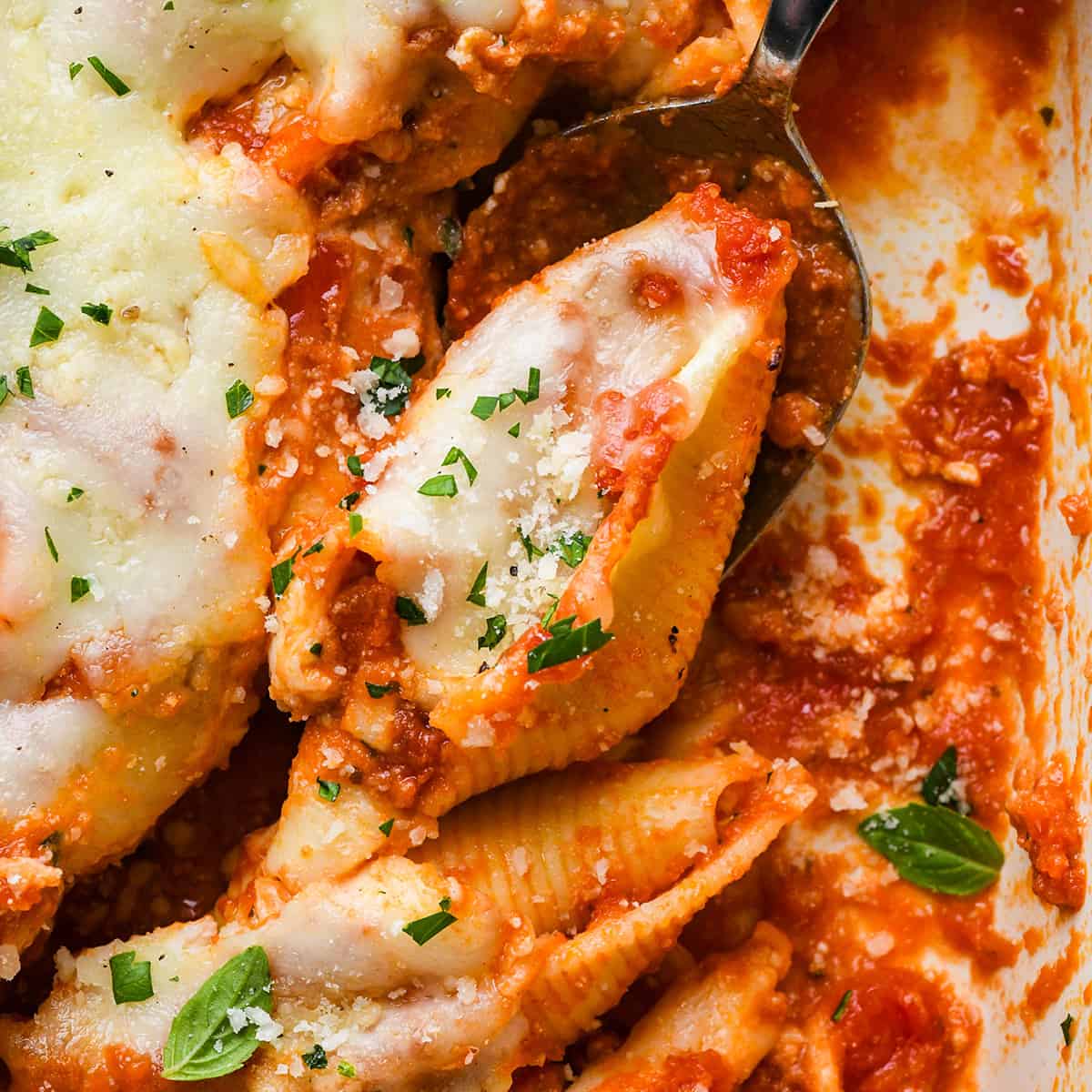 A spoon scooping Stuffed Shells out of a baking dish