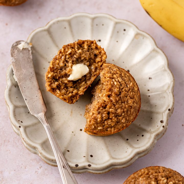 a Banana Oatmeal Muffin on a plate cut in half with butter on one half 