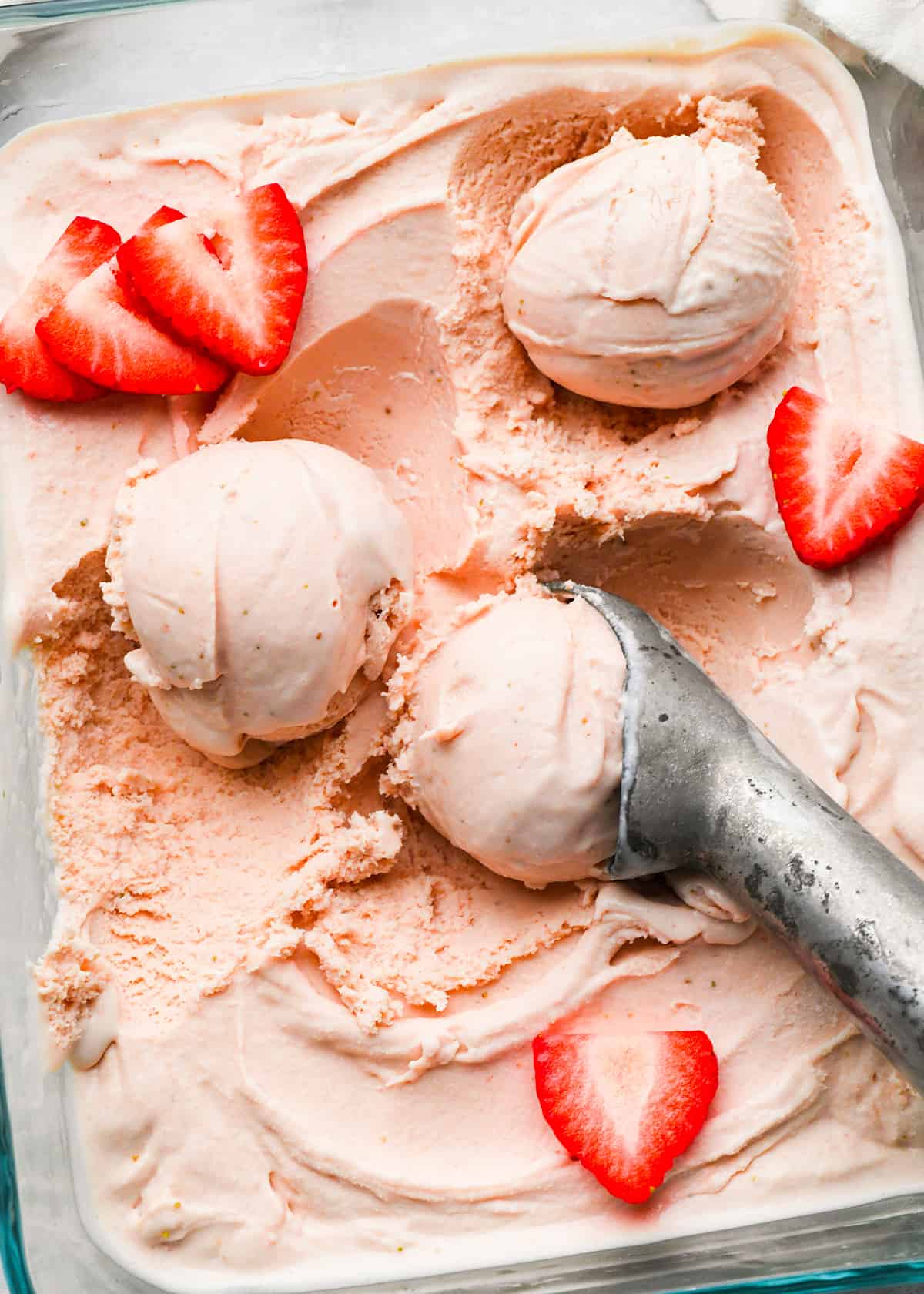 scoops of strawberry ice cream in a glass container with fresh strawberries